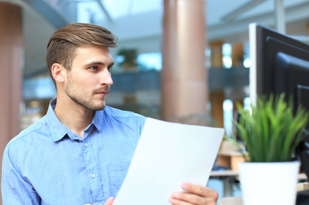 Joven empresario leyendo el papeleo en un escritorio en la oficina