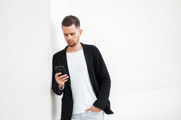 Joven empresario moderno con un teléfono móvil en ropa elegante en blanco