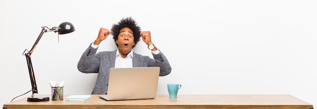 Joven empresario negro que celebra un éxito increíble como un ganador que parece emocionado y feliz diciendo ¡Toma eso!