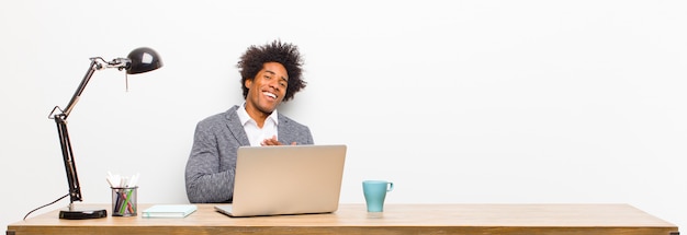 Joven empresario negro sintiéndose romántico, feliz y enamorado, sonriendo alegremente y tomados de la mano cerca del corazón en un escritorio