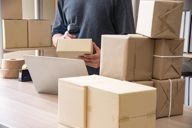 Foto joven empresario o empresario inteligente asiático propietario de una pyme de entrega en línea comprobando productos en existencias o paquetes joven propietario de pequeñas empresas que trabaja en su oficina en casa