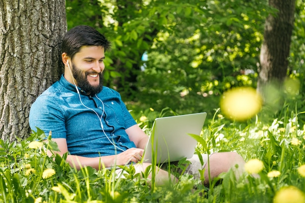 Joven empresario o estudiante en ropa casual usando la computadora portátil en el parque