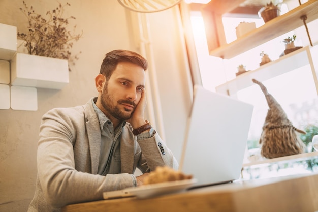 Joven empresario pensativo en un descanso en un café. Él está trabajando en la computadora portátil.