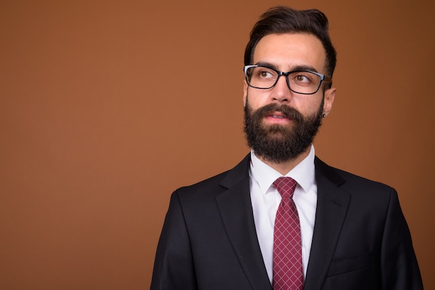 Joven empresario persa barbudo guapo en pared marrón