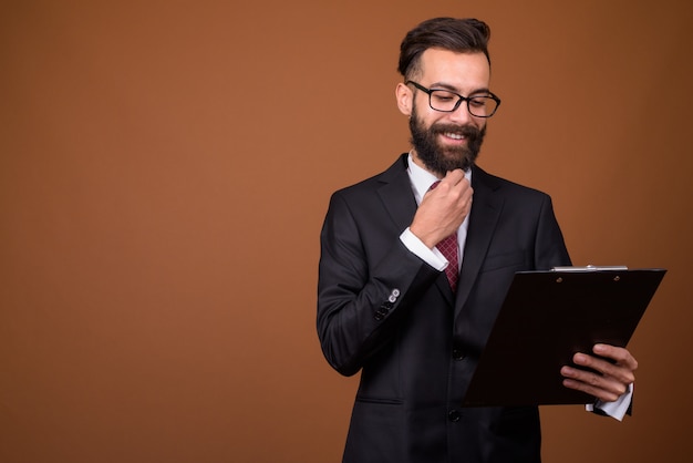 Joven empresario persa barbudo guapo en pared marrón