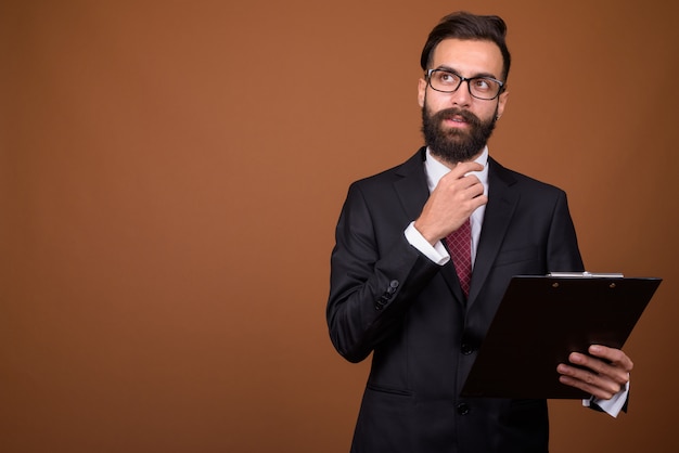 Joven empresario persa barbudo guapo en pared marrón