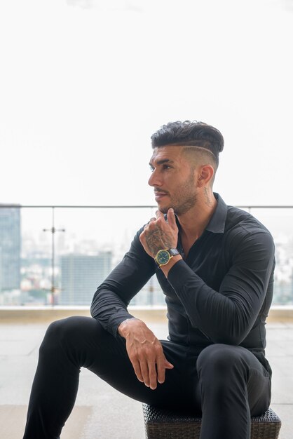 Joven empresario persa barbudo guapo pensando y sentado en la ciudad