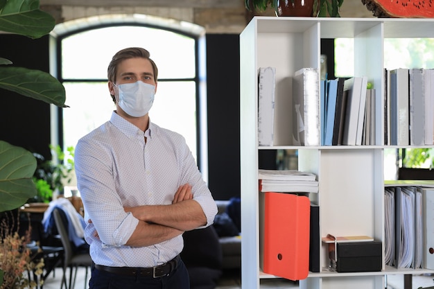 Joven empresario de pie de máscara médica en la oficina moderna.