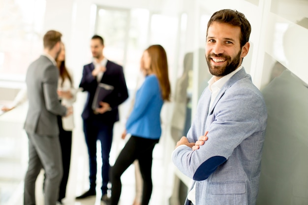 Foto joven empresario de pie en la oficina y otros jóvenes empresarios hablando en el fondo