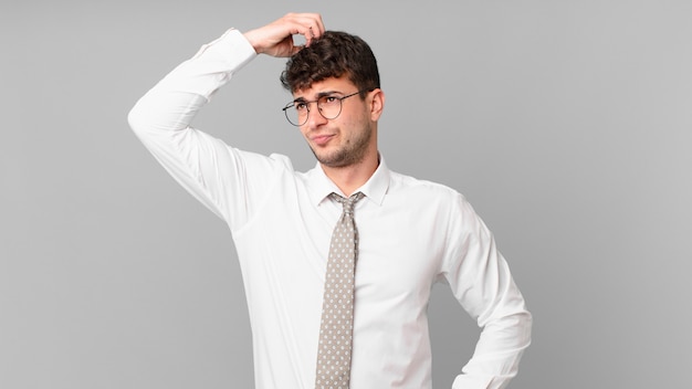 Foto joven empresario que se siente desconcertado y confundido, rascándose la cabeza y mirando hacia un lado