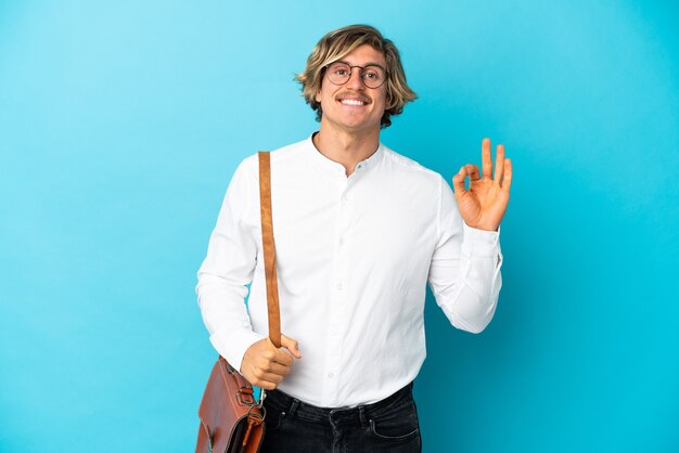 Joven empresario rubio aislado en la pared azul que muestra un signo de ok con los dedos