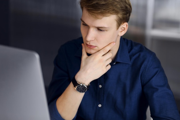 Joven empresario rubio sintiendo estrés en el lugar de trabajo en la oficina. El negocio de inicio significa trabajar duro y fuera de tiempo para lograr el éxito.