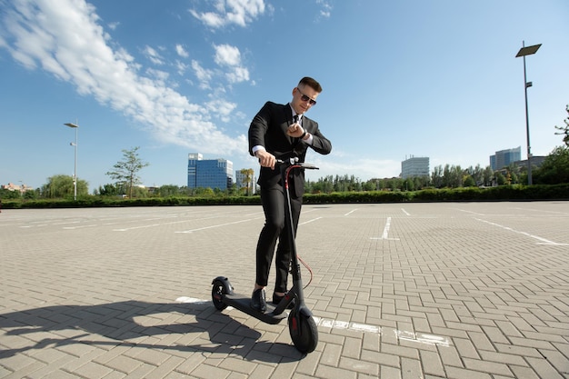 Joven empresario con scooter eléctrico de pie delante del edificio empresarial moderno