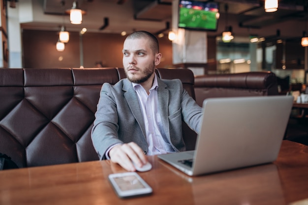 Joven empresario sentado en un café con una computadora portátil