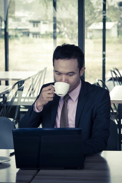 Joven empresario sentado en la cafetería, bebiendo café, con portátil