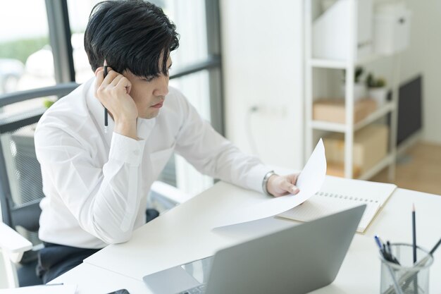 Joven empresario sentado en su escritorio mirando Internet en su computadora portátil Sintiéndose estresado