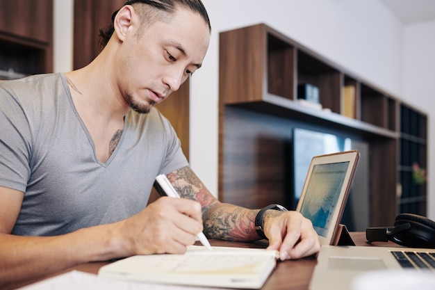 Joven empresario serio escribiendo planes e ideas en el bloc de notas cuando trabaja en su escritorio en casa