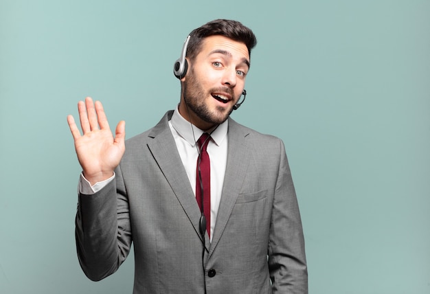 Joven empresario sonriendo feliz y alegremente, saludando con la mano, dándole la bienvenida y saludándolo, o diciendo adiós al concepto de telemarketing