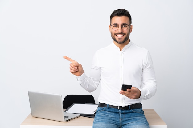 Joven empresario sosteniendo un teléfono móvil apuntando con el dedo al lado