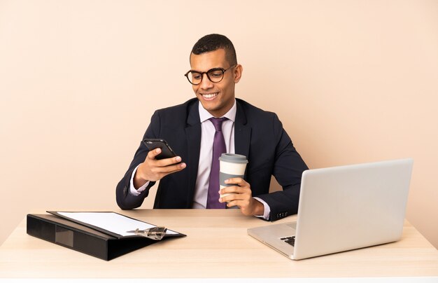 Joven empresario en su oficina con una computadora portátil y otros documentos con café para llevar y un móvil