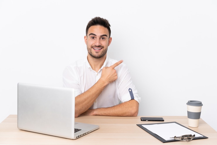 Foto joven empresario con un teléfono móvil en un lugar de trabajo apuntando con el dedo al lado