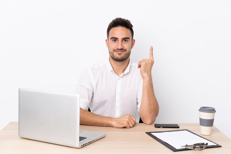 Foto joven empresario con un teléfono móvil en un lugar de trabajo señalando con el dedo índice una gran idea