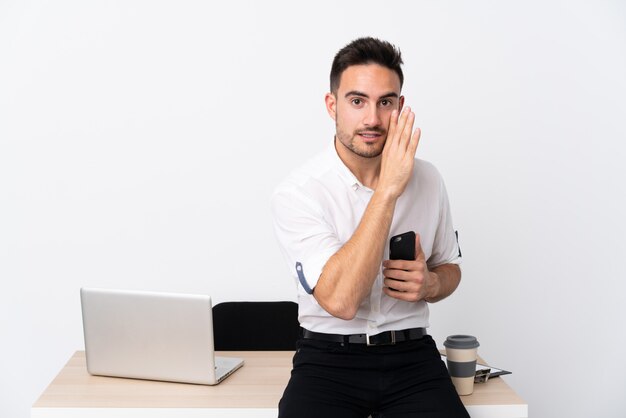 Joven empresario con un teléfono móvil en un lugar de trabajo susurrando algo