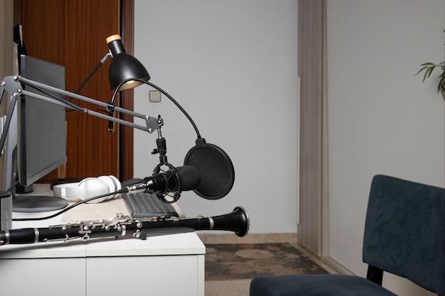 Joven empresario tocando el clarinete en casa y grabando música para transmitirla en línea con su computadora en el interior