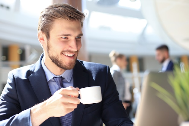 Joven empresario tomando café en la oficina mientras escribe en la computadora.