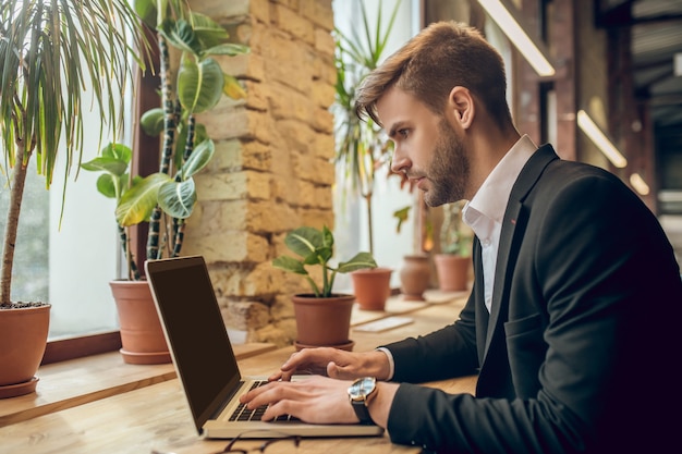 Joven empresario trabajando en el portátil en un café y mirando concentrado