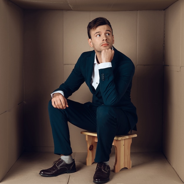 Joven empresario en traje negro en caja de cartón.