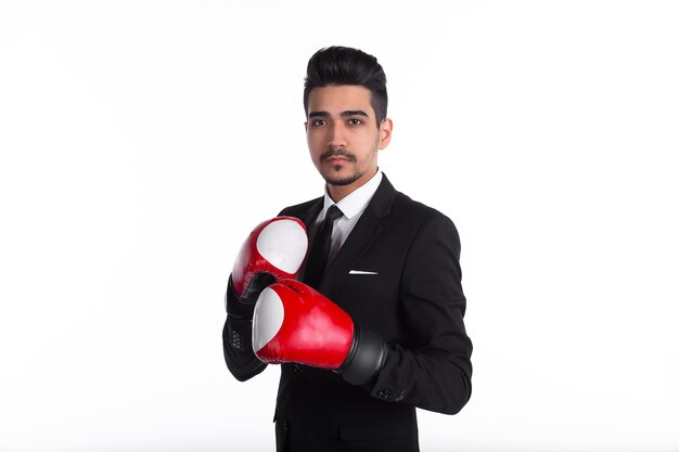 Joven empresario de traje negro y guantes de boxeo rojos aislado sobre fondo blanco.