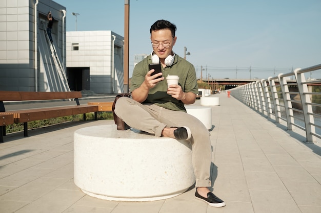 Joven empresario tranquilo tomando una copa y viendo videos en el teléfono inteligente