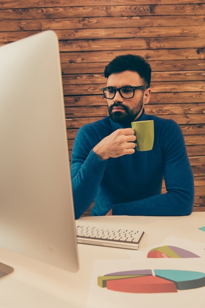 Joven empresario en vasos tomando café mientras trabaja en el pc