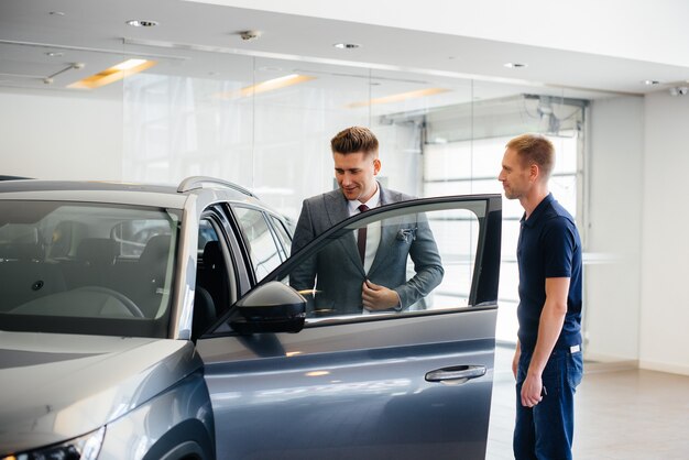 Un joven empresario con un vendedor mira un coche nuevo en un concesionario de coches