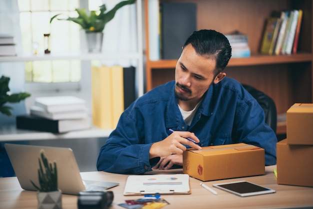 Joven empresario vendiendo productos en línea sentado sonriendo felizmente en su lugar de trabajo.