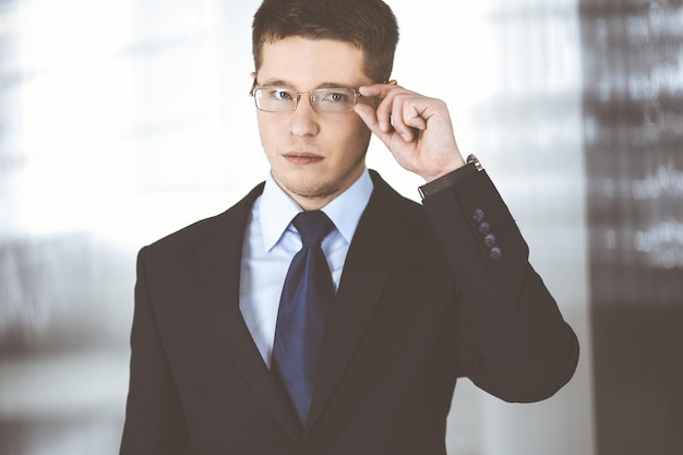 Joven empresario vestido con traje, con gafas, mientras está de pie en la oficina. Concepto de éxito empresarial hoy en día.