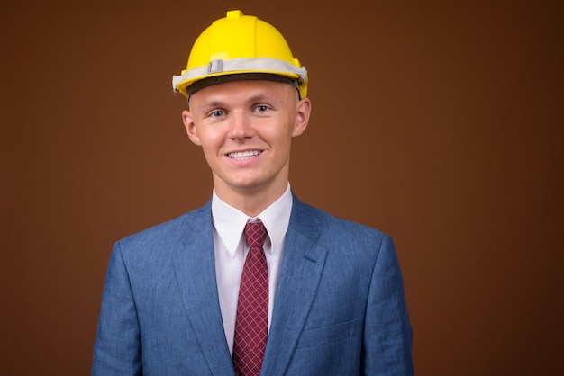 Joven empresario vistiendo casco contra el fondo marrón