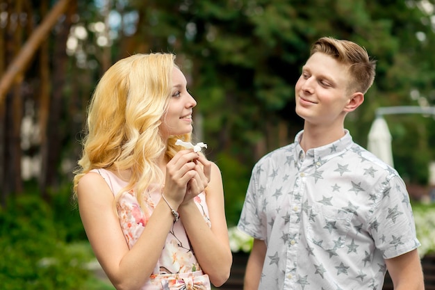 Joven encantadora chica rubia está coqueteando y con un chico en el jardín. Amor de una pareja enamorada