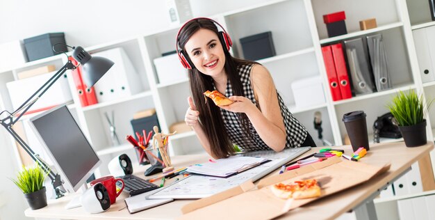 Una joven se encuentra cerca de una mesa, sostiene un pedazo de pizza en la mano y muestra un cartel de clase.