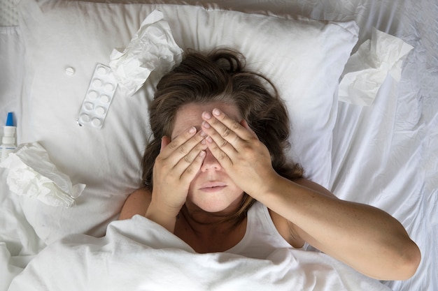 Foto una joven enferma en la cama, acostada con la cabeza debajo de las mantas y un montón de pañuelos junto a ella