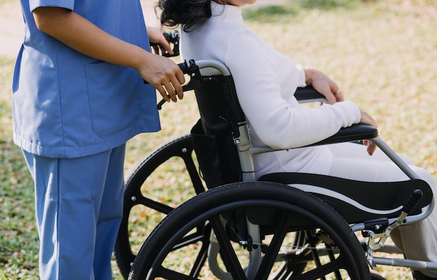 Una joven enfermera asiática en un hogar de ancianos cuida a un anciano discapacitado. El médico cuidador sirve fisioterapia para que los pacientes mayores hagan ejercicio y practiquen caminar con andador o bastón en el patio trasero.