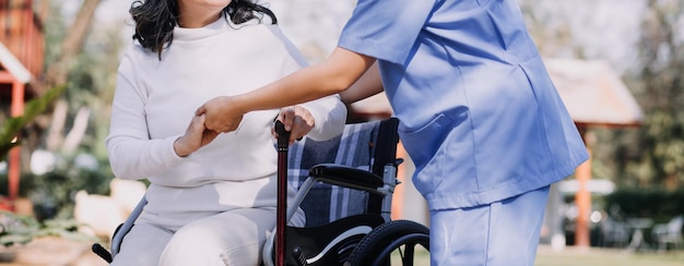 Una joven enfermera asiática en un hogar de ancianos cuida a un anciano discapacitado. El médico cuidador sirve fisioterapia para que los pacientes mayores hagan ejercicio y practiquen caminar con andador o bastón en el patio trasero.