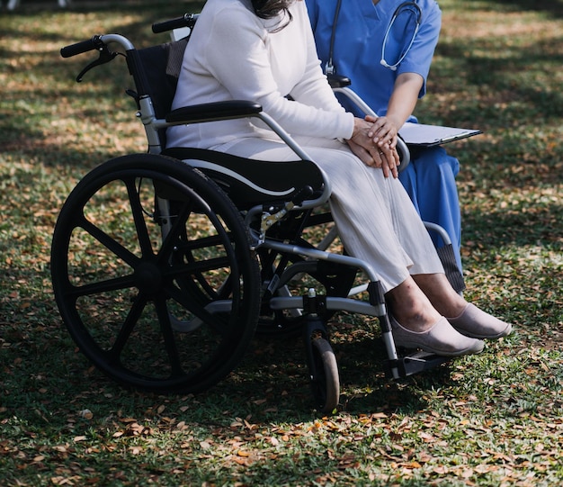 Una joven enfermera asiática en un hogar de ancianos cuida a un anciano discapacitado. El médico cuidador sirve fisioterapia para que los pacientes mayores hagan ejercicio y practiquen caminar con andador o bastón en el patio trasero.