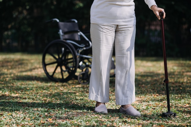 Una joven enfermera asiática en un hogar de ancianos cuida a un anciano discapacitado. El médico cuidador sirve fisioterapia para que los pacientes mayores hagan ejercicio y practiquen caminar con andador o bastón en el patio trasero.