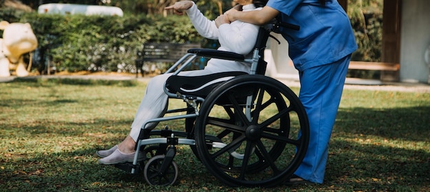 Una joven enfermera asiática en un hogar de ancianos cuida a un anciano discapacitado. El médico cuidador sirve fisioterapia para que los pacientes mayores hagan ejercicio y practiquen caminar con andador o bastón en el patio trasero.