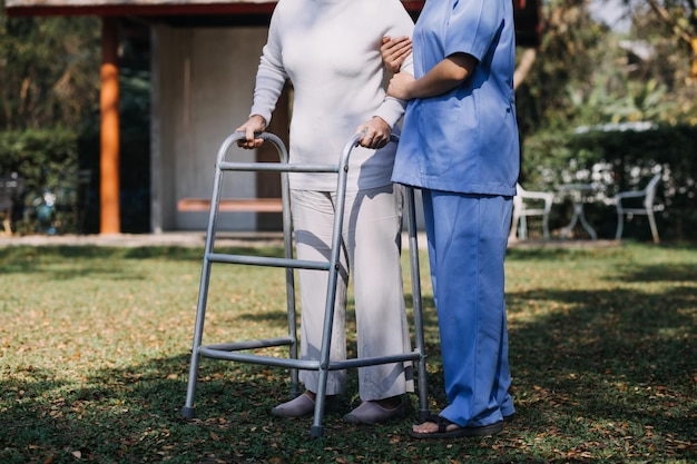 Foto una joven enfermera asiática en un hogar de ancianos cuida a un anciano discapacitado. el médico cuidador sirve fisioterapia para que los pacientes mayores hagan ejercicio y practiquen caminar con andador o bastón en el patio trasero.
