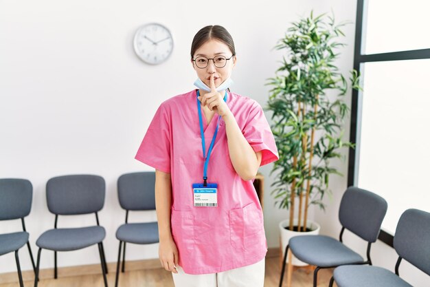 Joven enfermera asiática en la sala de espera médica pidiendo silencio con el dedo en los labios silencio y concepto secreto