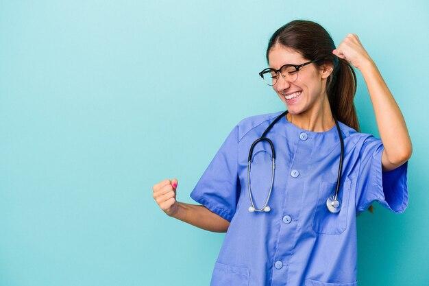 Joven enfermera caucásica aislada sobre fondo azul levantando el puño después de una victoria, concepto ganador.