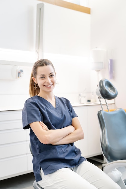 Joven enfermera con chaqueta azul sonríe en el consultorio dental antes de recibir al paciente